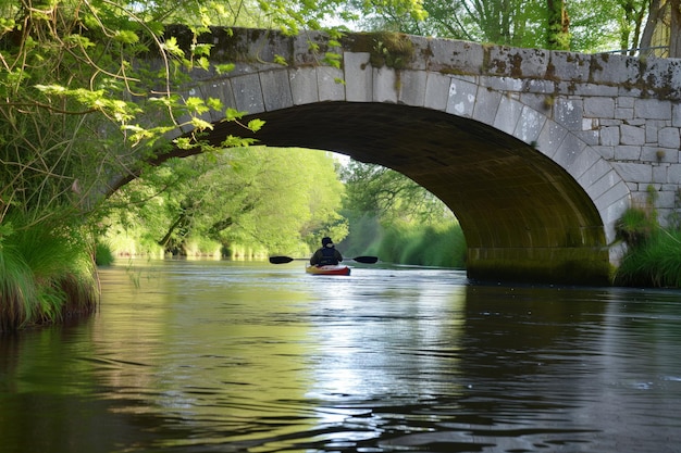 Un kayakista pasando bajo un puente de piedra sobre un río tranquilo