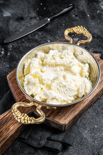 Kaymak Creme coagulado, creme de manteiga em uma frigideira rústica. Fundo preto. Vista do topo.