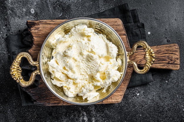 Kaymak Creme coagulado, creme de manteiga em uma frigideira rústica. Fundo preto. Vista do topo.