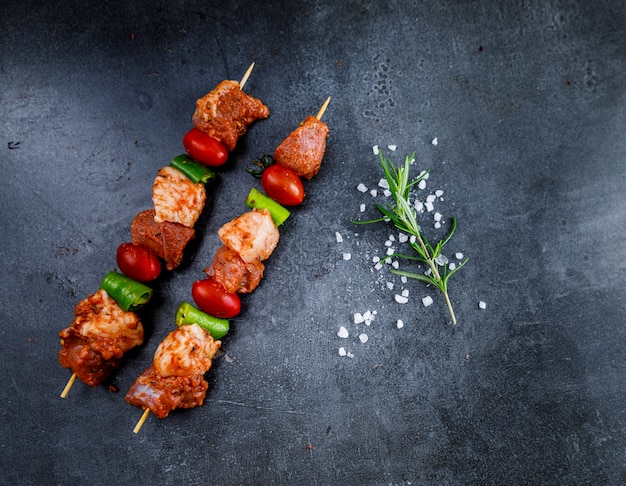 Kebab de carne cruda cerca de sal y romero en el fondo oscuro