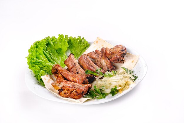 Kebab de carne sobre costillas sobre lavash con cebolla y repollo en un plato blanco, sobre un fondo blanco aislado