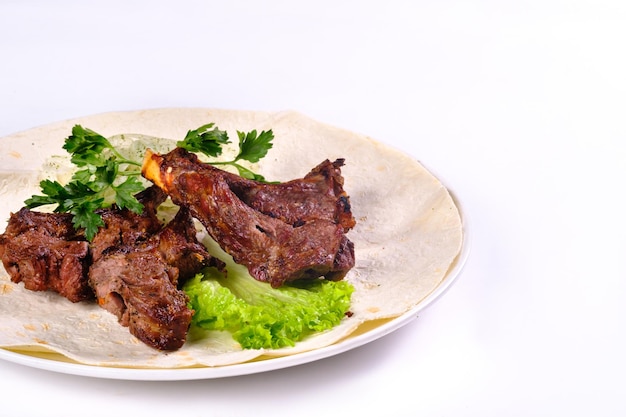 Kebab de carne sobre costillas sobre lavash con cebolla y repollo en un plato blanco, sobre un fondo blanco aislado.