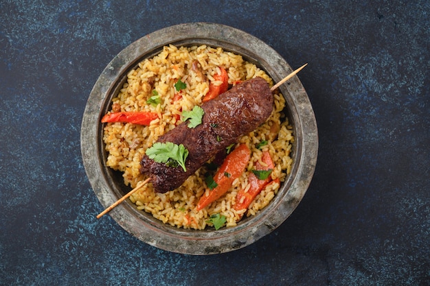 Kebab de carne tradicional del Medio Oriente con arroz en placa de metal rústico en la vista superior de fondo rústico azul. Comida árabe para el almuerzo o la cena, cocina de Oriente Medio.