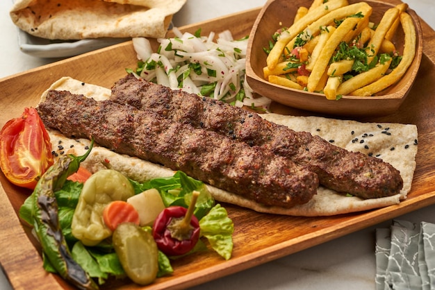 Kebab de cordero con papas fritas, pan de pita y lima servido en un plato aislado en la vista lateral de fondo gris de la comida rápida