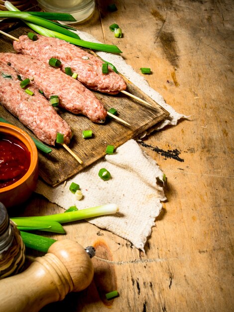 Kebab crudo con salsa de tomate y cebollas verdes en mesa de madera.