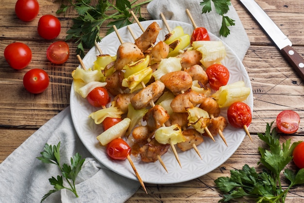 Kebab de frango, abobrinha e tomate no espeto em um prato.