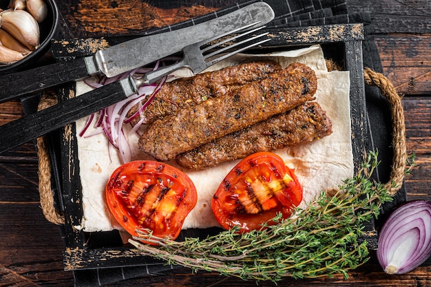 Kebab de urfa turca em uma bandeja de madeira com pão, cebola e tomate. fundo de madeira. vista do topo.