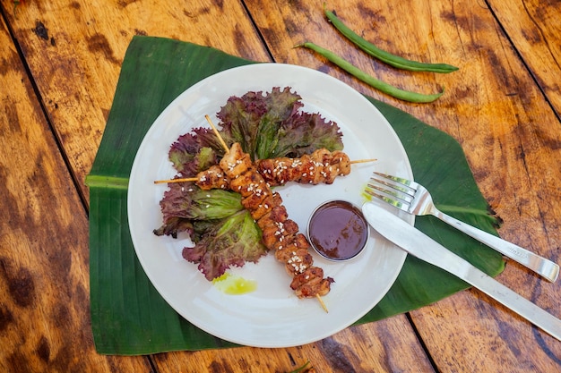 Kebab de estilo tropical asiático en el plato con hojas de plátano y lechuga y semillas de sésamo en la mesa de madera