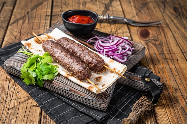 Kebab kofta kefta tradicional de Oriente Medio de carne molida de res y cordero a la parrilla en brochetas servidas con pan plano y cebolla Fondo de madera Vista superior