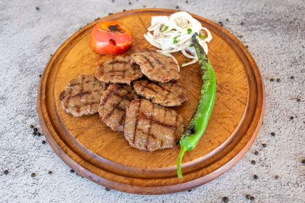 Kebab kofte o albóndigas sobre fondo de madera con pimientos asados tomates y cebollas