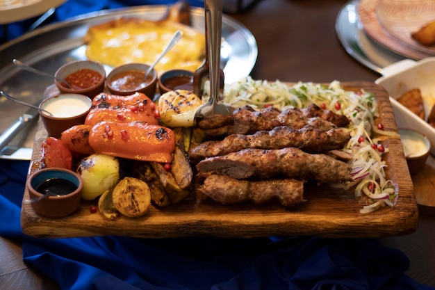 Kebab a la parrilla con especias y salsas de verduras a la parrilla y cebollas frescas con granada Una gran porción para una gran empresa en el restaurante en un plato rectangular de madera