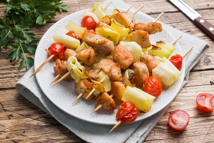 Foto kebab de pollo, calabacín y tomates en brochetas en un plato.