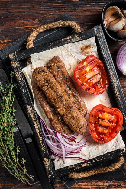 Kebab turco de urfa en una bandeja de madera con pan, cebolla y tomate Vista superior de fondo de madera