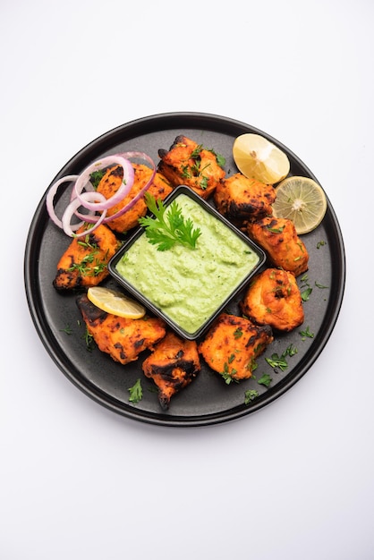 Kebabs tikka de frango indiano, marinado em especiarias e iogurte e assado em tandoor. servido com chutney verde e cebola. foco seletivo