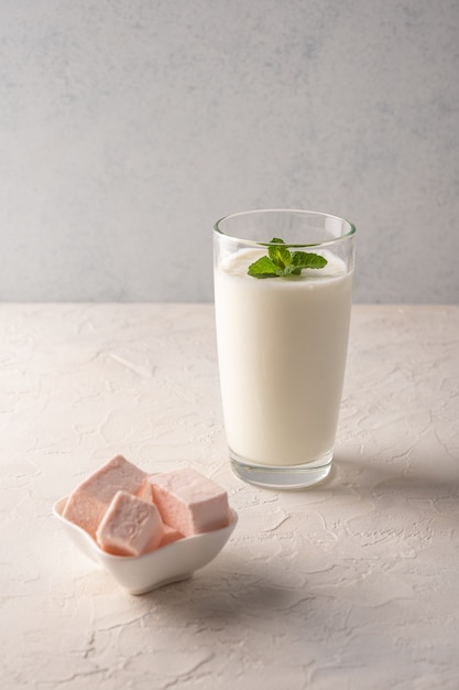 Kefir mit kräutern in einem glas und pastille auf einem hellen hintergrund. vertikale ausrichtung.