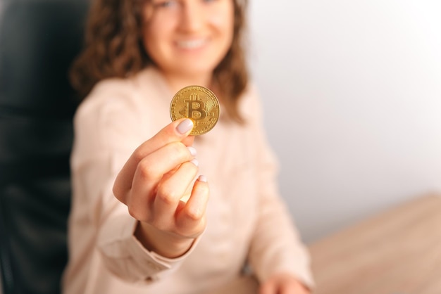 Kein Gesichtsfoto einer jungen Frau, die der Kamera einen goldenen Bitcoin zeigt Unscharfer Hintergrund