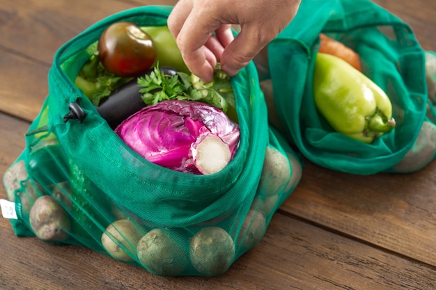 Kein Plastiktütekonzept. Mascheneinkaufstüten des sortierten Gemüses auf Holztisch