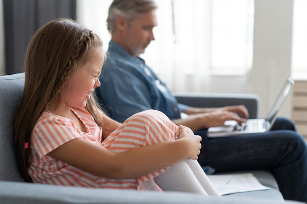 Keine Zeit für Kinder. Grauhaariger Vater beschäftigt mit Laptop, arbeitet online zu Hause, traurige gelangweilte beleidigte Tochter sitzt in der Nähe.