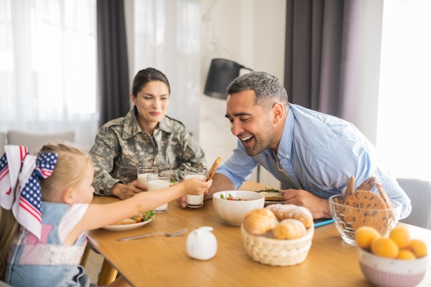 Keks für Papa. Schönes, großzügiges Mädchen, das Papa beim Frühstück mit der Familie ihren Keks gibt