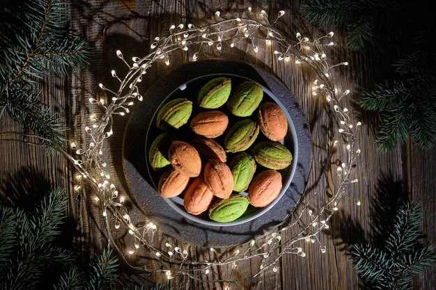 Kekse in Walnussform mit Dulce De Leche Leckeres Dessert auf dunklem Hintergrund mit natürlichem Weihnachtsdekor Tannenzweige auf dunklem rustikalem Holz Festliche Lichtergirlande im Kreis um den Teller