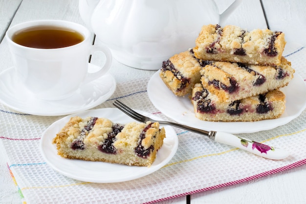 Kekse mit Blaubeermarmelade Teekanne und Tasse Tee auf weißem Hintergrund