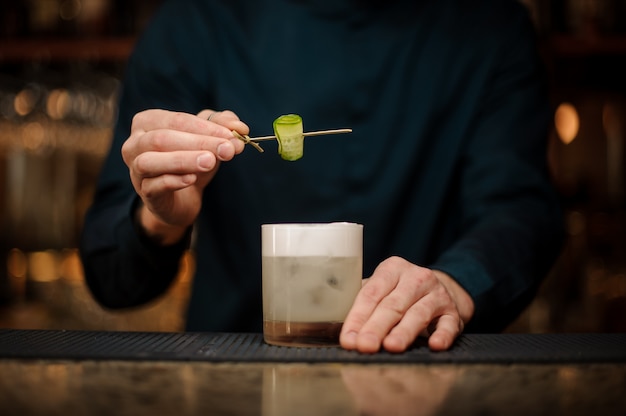 Kellner, der ein Cocktailglas mit einer Gurke auf einer hölzernen Aufsteckspindel verziert