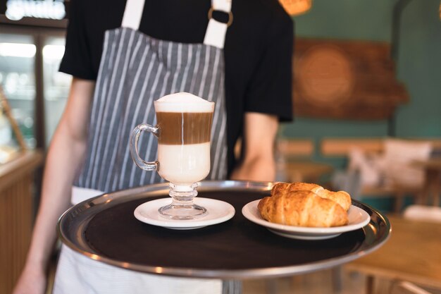 Kellner, der ein Tablett mit frischen Croissants und Kaffee hält.