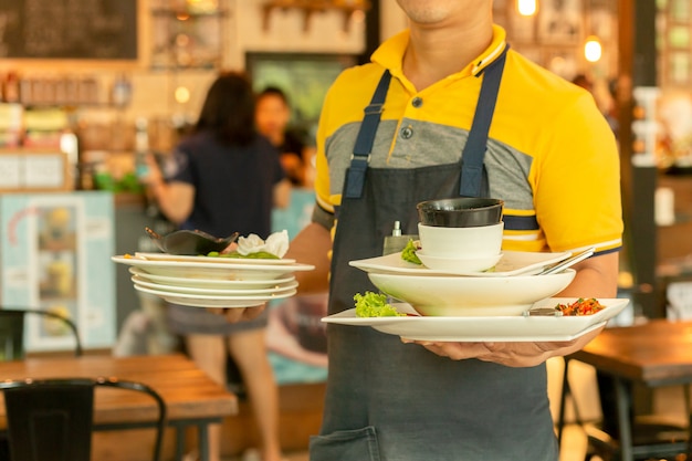 Kellner, der schmutzige Teller von den Tabellen im Restaurant entfernt.