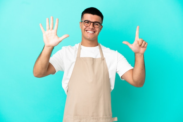 Kellner im Restaurant über isoliertem blauem Hintergrund, der mit den Fingern sieben zählt