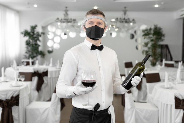 Kellner in einer Schutzmaske mit einem Glas Rotwein in den Händen