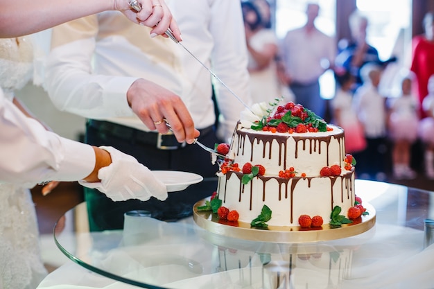 Kellner nimmt ein Stück Hochzeitstorte, während Braut und Bräutigam es schneiden