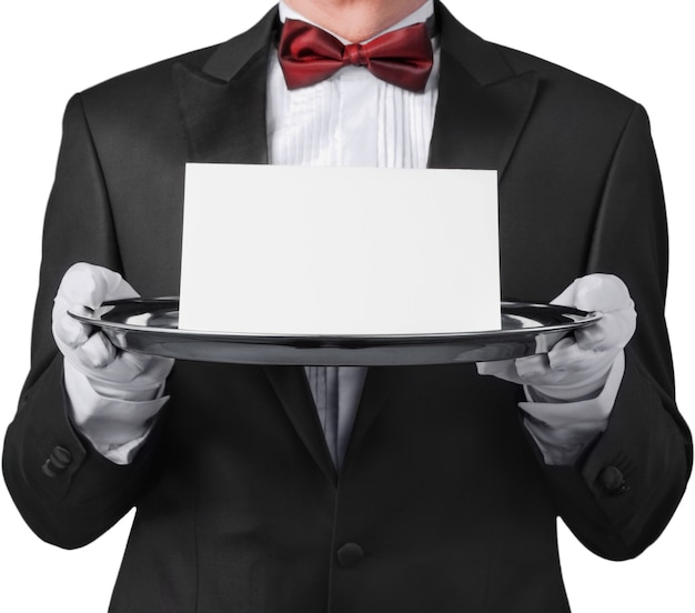 Kellner oder Butler, der einen Smoking trägt und eine Notizkarte auf einem silbernen Tablett vor seinem Oberkörper hält.