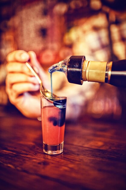 Kellner schenkt Cocktailgetränk in Schnapsgläser an der Theke ein