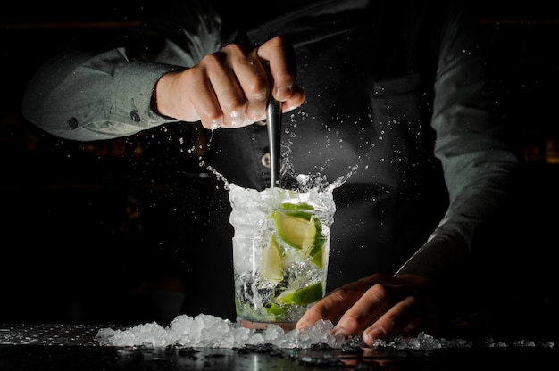 Kellnerhand, die frischen saft vom kalk macht den caipirinha-cocktail zusammendrückt