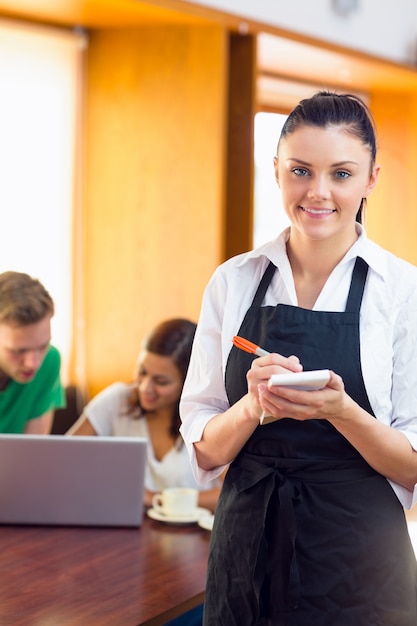 Kellnerin, die einen Auftrag mit den Studenten verwenden Laptop an der Kaffeestube schreibt