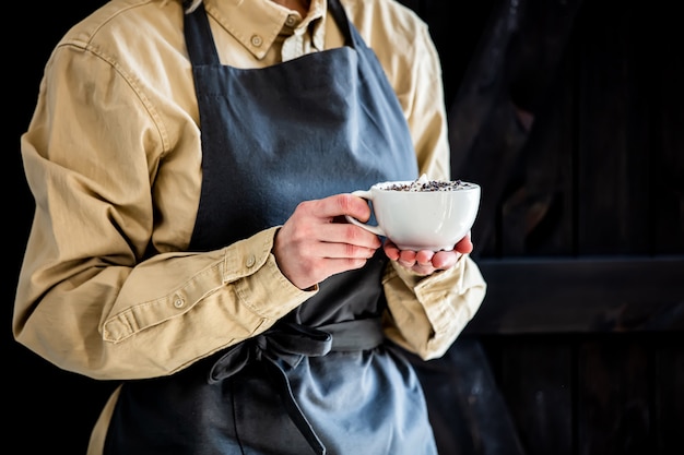 Kellnerin in einer Schürze hält einen Cappuccino