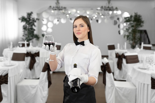 Kellnerin in weißen Handschuhen hält ein Glas und eine Flasche Rotwein