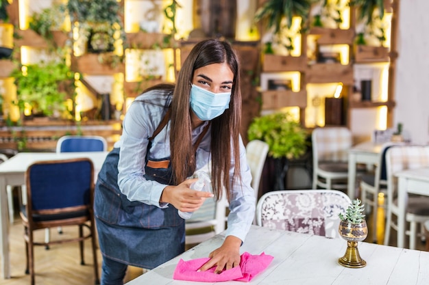 Kellnerin trägt eine Schutzmaske, während sie die Tische in Restaurants oder Cafés für den nächsten Kunden desinfiziert Corona-Virus und kleine Unternehmen sind für die Arbeit offen Konzept