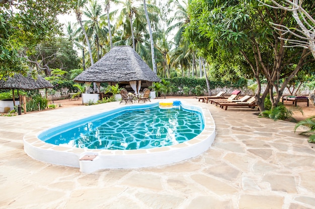 Foto kenia. piscina de lujo en el jardín africano con sillas típicas locales hechas de madera en el fondo