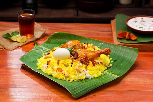 Kerala Chicken Biryani traditionell angerichtet in einem Bananenblatt und Raita als Beilage