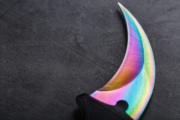 Kerambit-Dolch mit regenbogenfarbener Klinge auf dunklem strukturiertem Hintergrund. Kalte Waffen, freier Speicherplatz