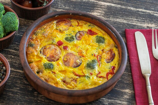 Keramikschale mit Gemüsefrittata einfaches vegetarisches Essen Frittata mit Ei Tomate Paprika Zwiebel Brokkoli und Käse auf Holztisch Italienisches Eieromelett