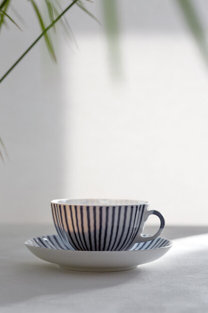 Keramiktasse weiß mit blauem Muster auf dem Tisch Natürliche Beleuchtung helle Sonne aus dem Fenster