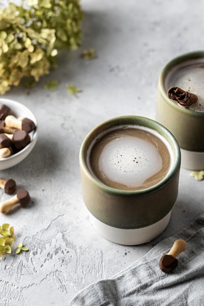 Keramiktassen mit Kaffeecappuccino mit Schaum mit Keksserviette und Blumen auf strukturiertem Hintergrund