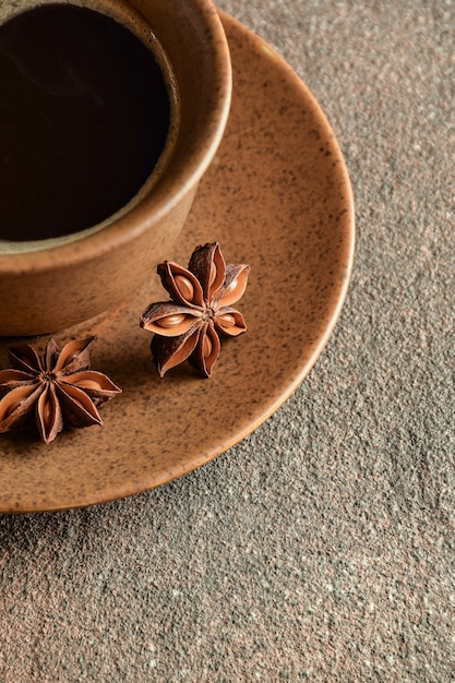 Keramische braune Kaffeetasse mit Untertasse und Anis liegen auf einer steinernen Hintergrundnahaufnahme. Rechts ist Platz für eine Inschrift