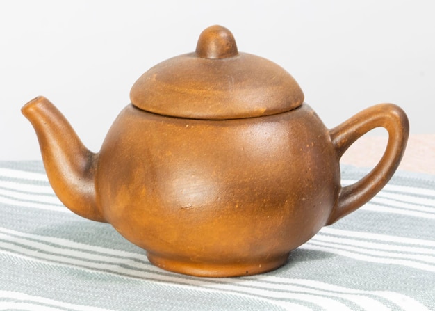 Keramische braune Teekanne steht auf einem weißen Hintergrund des Tisches