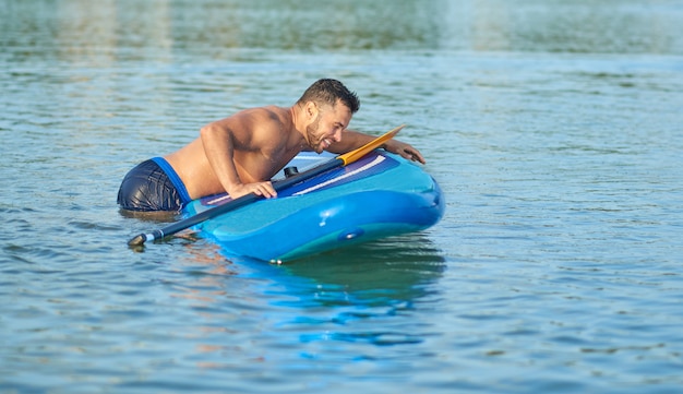 Kerl, der am Paddelbrett aus dem Wasser springt, nachdem er in Stadtsee gefallen ist.