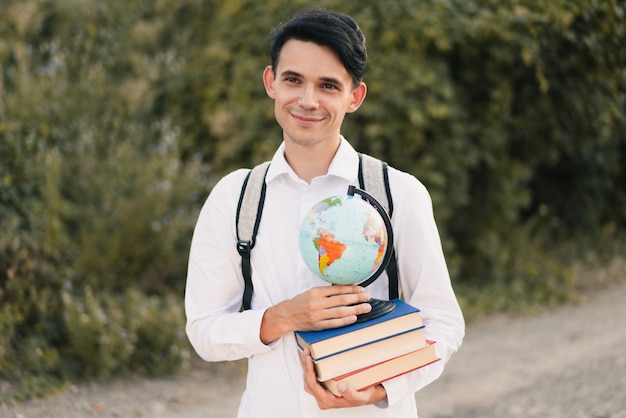 Kerl, der einen Stapel Bücher mit einem Globus hält