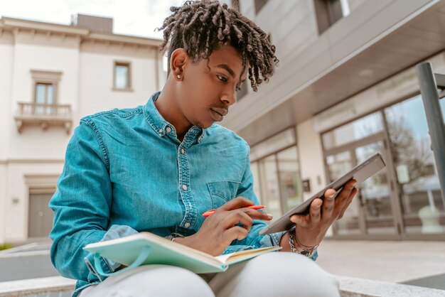 Foto kerl, der tablet sitzt mit notizblock und stift betrachtet