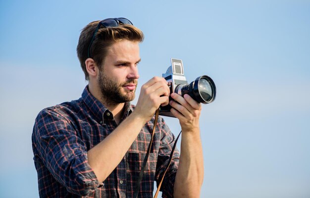 Kerl im Freien blauer Himmel Hintergrund Fotojournalist Konzept Reiseblogger Reporter, der Foto macht Vintage-Ausrüstung Blogger schießt vlog Urlaubszeit Hübscher Blogger-Typ Reisender Retro-Kamera